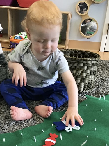 An infant is placing felt decorations onto a felt christmas tree.