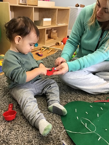 An infant and an educator are holding a felt decorations and examining it.