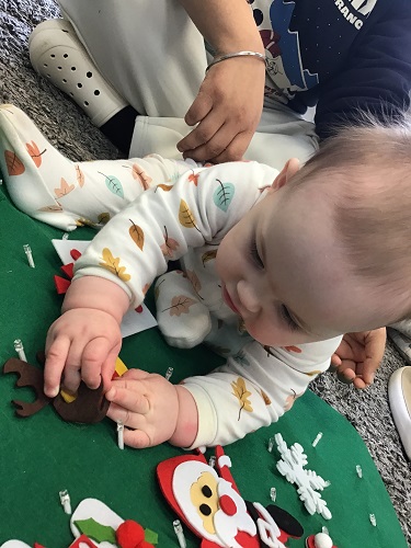 An infant is placing felt decorations onto a felt christmas tree.