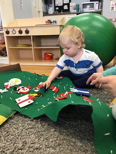 An infant is placing felt decorations onto a felt christmas tree.