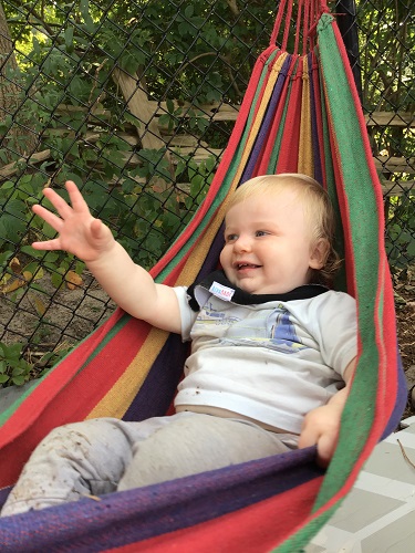 An infant is sitting the a hammock and reaching out.