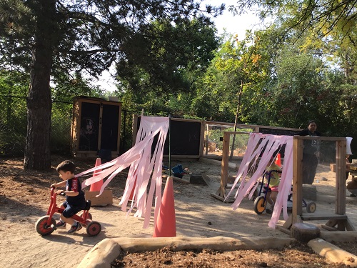 Some preschoolers are riding their bikes through pieces of fabric that is part of their car wash.