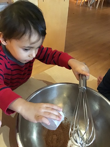 A preschooler is dumping ingredients to make hot chocolate into a bowl.
