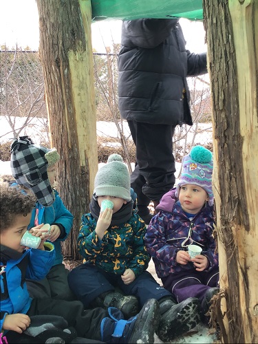 Several preschoolers are sitting in their fort, drinking hot chocolate.