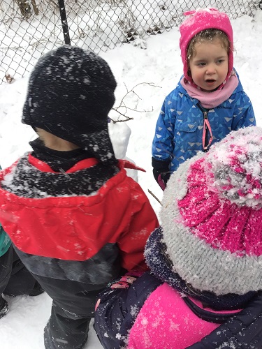 Several preschoolers are standing around their snowman.