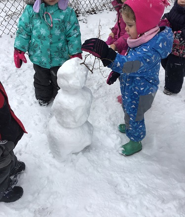 A preschooler is adding a skinny tree branch to their snowman.