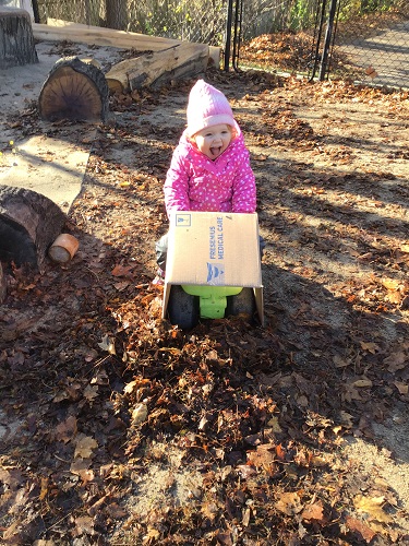 A toddler is riding on a car with a box on the front.