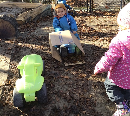 A toddler is riding on a car with a box on the front.