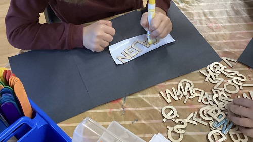 School Age 1 child colouring the wooden letters of their name