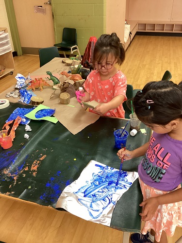 2 kindergarten children painting tin foil to represent a sea scene