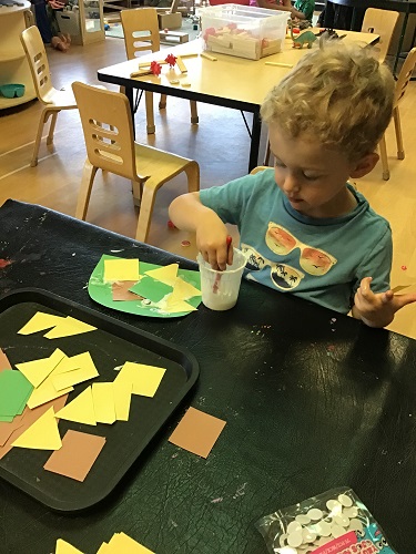 preschool boy creating dinosaur with paper shapes 