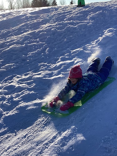 school-age child sledding down hill