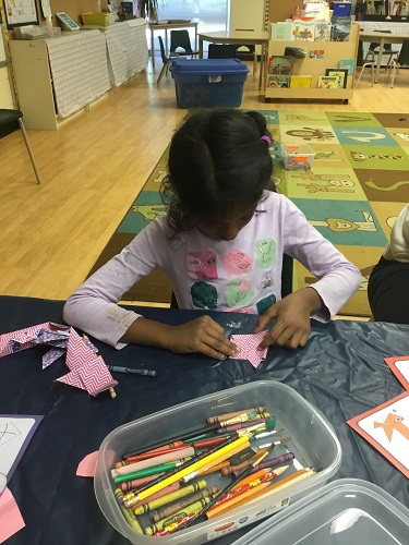 school-age girls creating boat with origami 