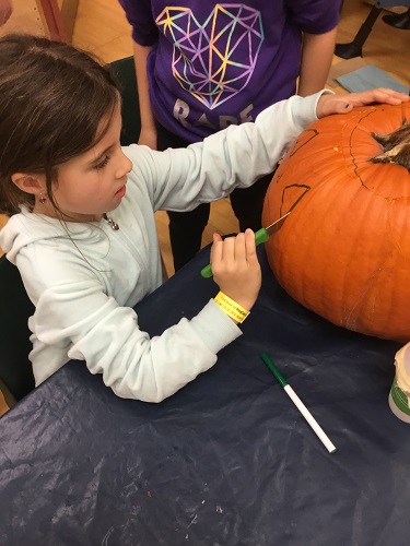 school-age girl carving eye out of pumpkin