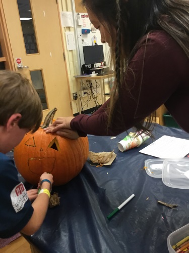 Educator and school-age children finishing pumpkin together 