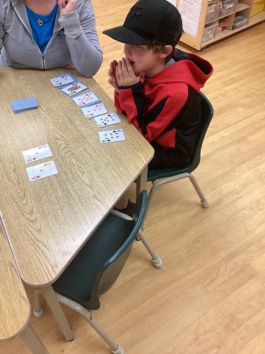School-age boy learning Solitaire with educator