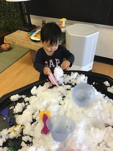 Toddler exploring the coloured snow in tuff tray