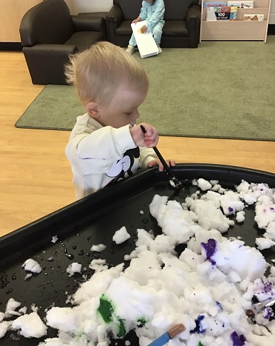 Toddler scooping snow with scoop
