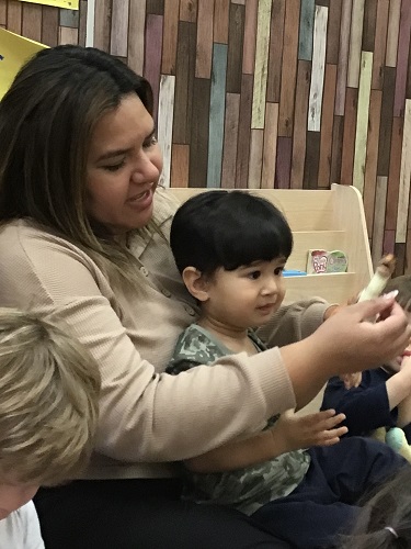 educator sitting with toddler child showing off his toy from home 