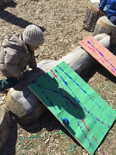 preschool boy rolling wheel through paint on paper 