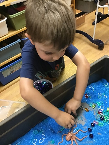 Kindergarten boy sifting through blue sand