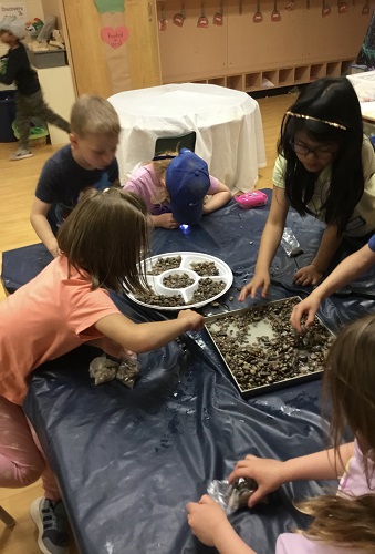 group of school-age children looking through rocks