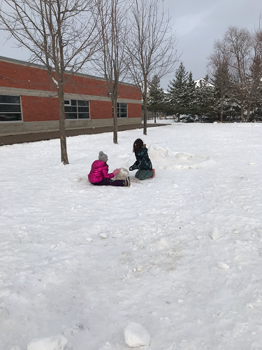 2 school-age girls working together to roll a boulder