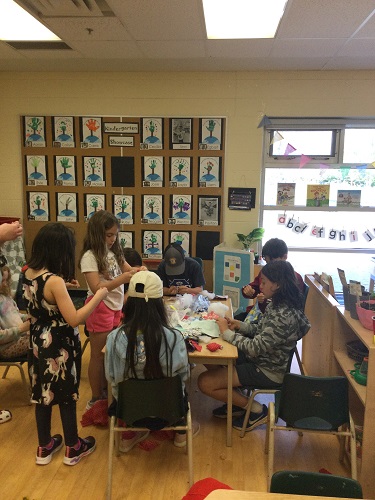 A group of school age children gathered at table sewing together 