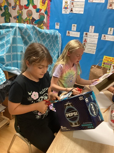 2 school-age girls cutting up boxes for their structure 