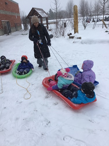 educator pulling toddlers on sled