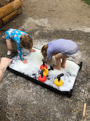 Two toddlers are are using their whole bodies to feel and Ooblek.