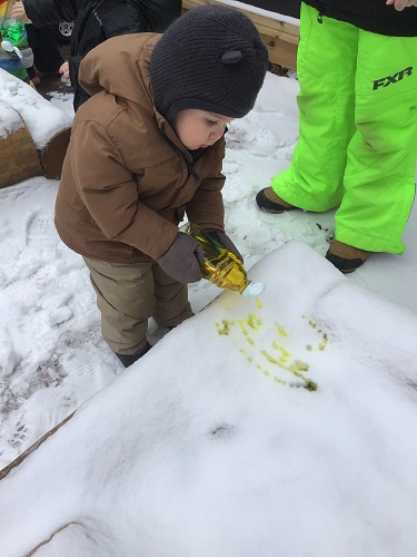 A preschooler is squirting paint into some snow outside.