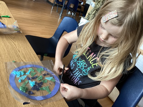 A school age child using scissors to cut out the sticky tape around their world sun catcher