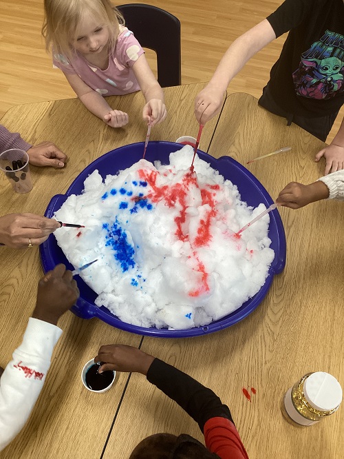 A group of school age children using pipettes and coloured water on a tray of snow