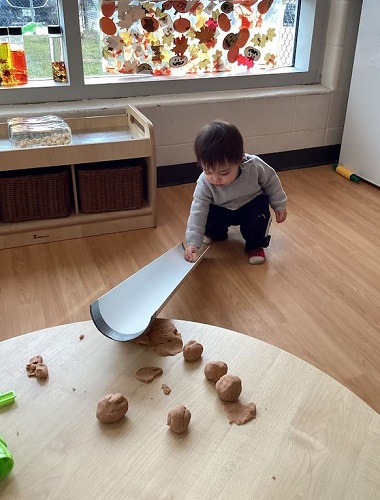 A child rolling play dough down a ramp