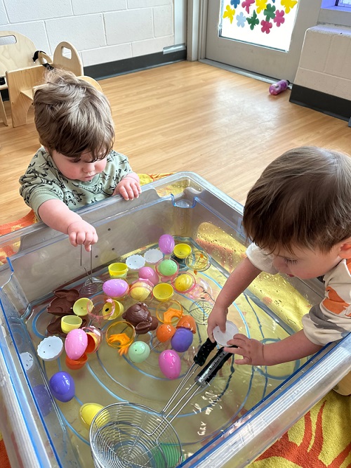 Children exploring with scoops in water and plastic eggs.