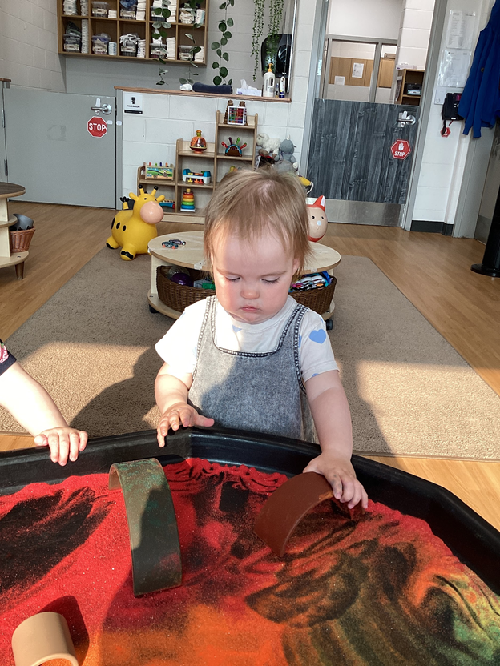 A child exploring a rainbow filled tuff tray.