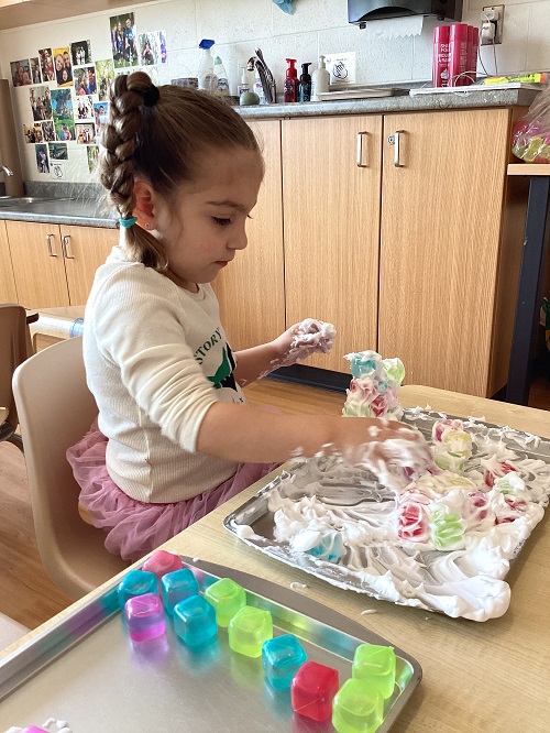 A child exploring with shaving foam and loose parts.