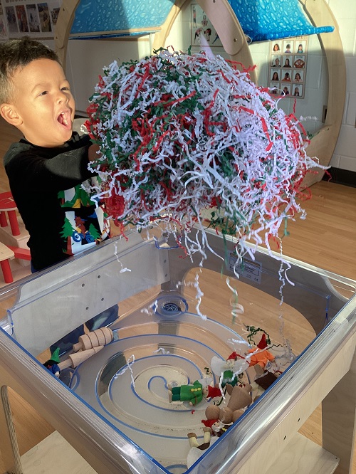 A child excitedly holding items from the sensory bin.