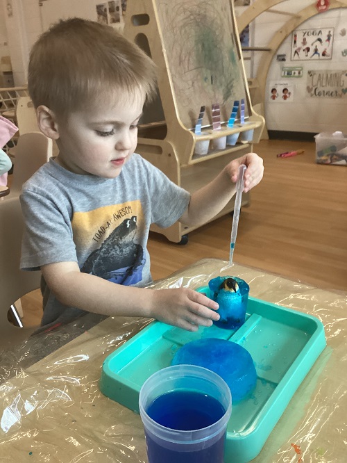 A child using a water dropper on their frozen treasure