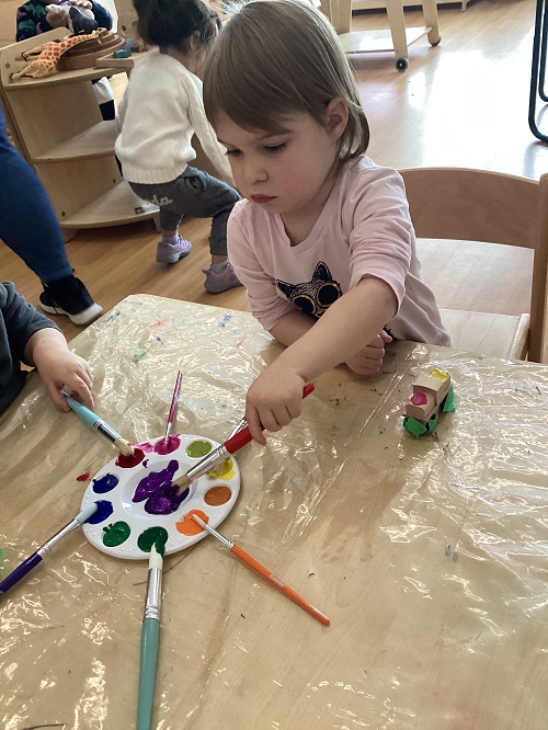 A child sitting while dipping a paintbrush into paint