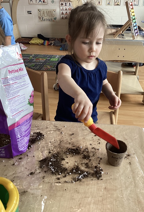 A child scooping soil into their planter cup.