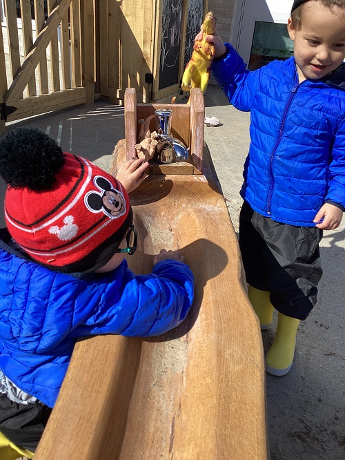 Two children exploring the water trough with dinos