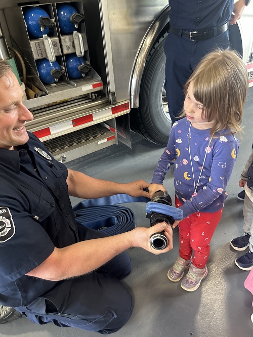A fire fighter assisting a child while holding a fire hose.