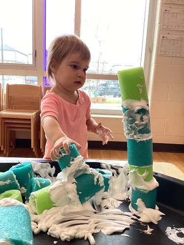 A child building a tower with the shaving cream covered pool noodles.