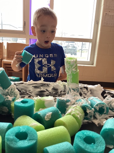 A child building a tower with the shaving cream covered pool noodles.