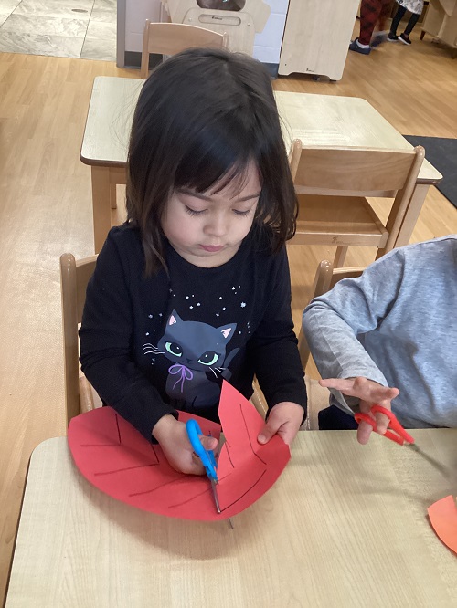 A child using scissors to cut a paper leaf