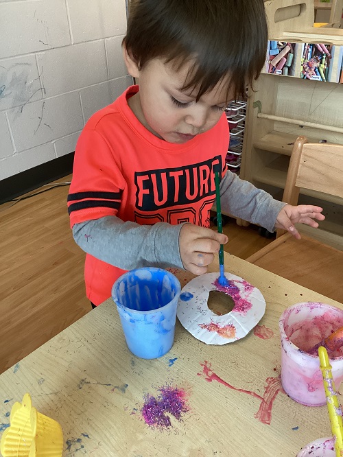 A child standing and painting a donut shaped piece of paper