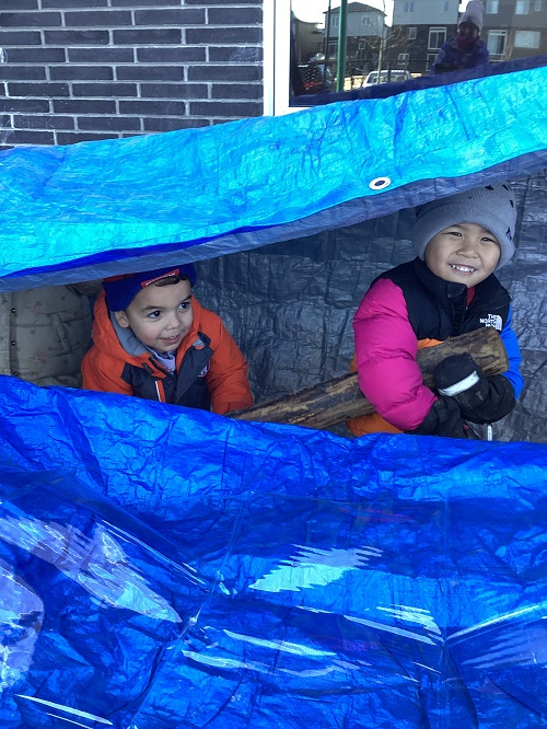 Two children sitting under a tarp on the playground