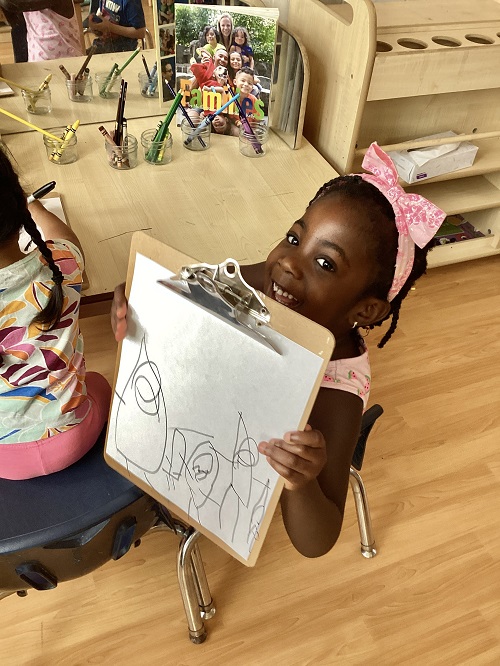 A child smiling as they show their picture of their family